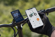 A smart bike computer mounted on a bicycle handlebar next to a gloved hand holding a smartphone showing the Engwe App interface for a folding bike. Text at the top reads 'Smarter App Connectivity' and mentions Bluetooth and the Engwe App.