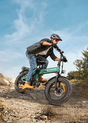Person riding a green electric bike on a dirt path with a clear blue sky.