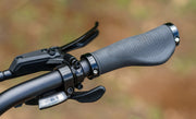 Close-up of a bicycle handlebar with grip and brake lever against a blurred natural background