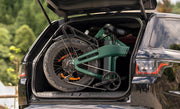 Green bicycle folded and loaded into the trunk of a black car with a blurred natural background