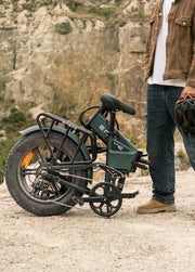 Person standing next to a folded electric bike in a rocky outdoor setting