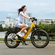 Woman riding a yellow electric bike on a city street with buildings and greenery in the background