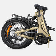 A folding electric bicycle shown from a rear three-quarter angle on a light gray studio background. The frame is a warm champagne gold color with black components, a black saddle, black tires, and small orange accents on the wheel spokes.