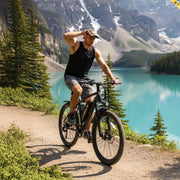 Man riding a bicycle on a trail near a lake with mountains in the background